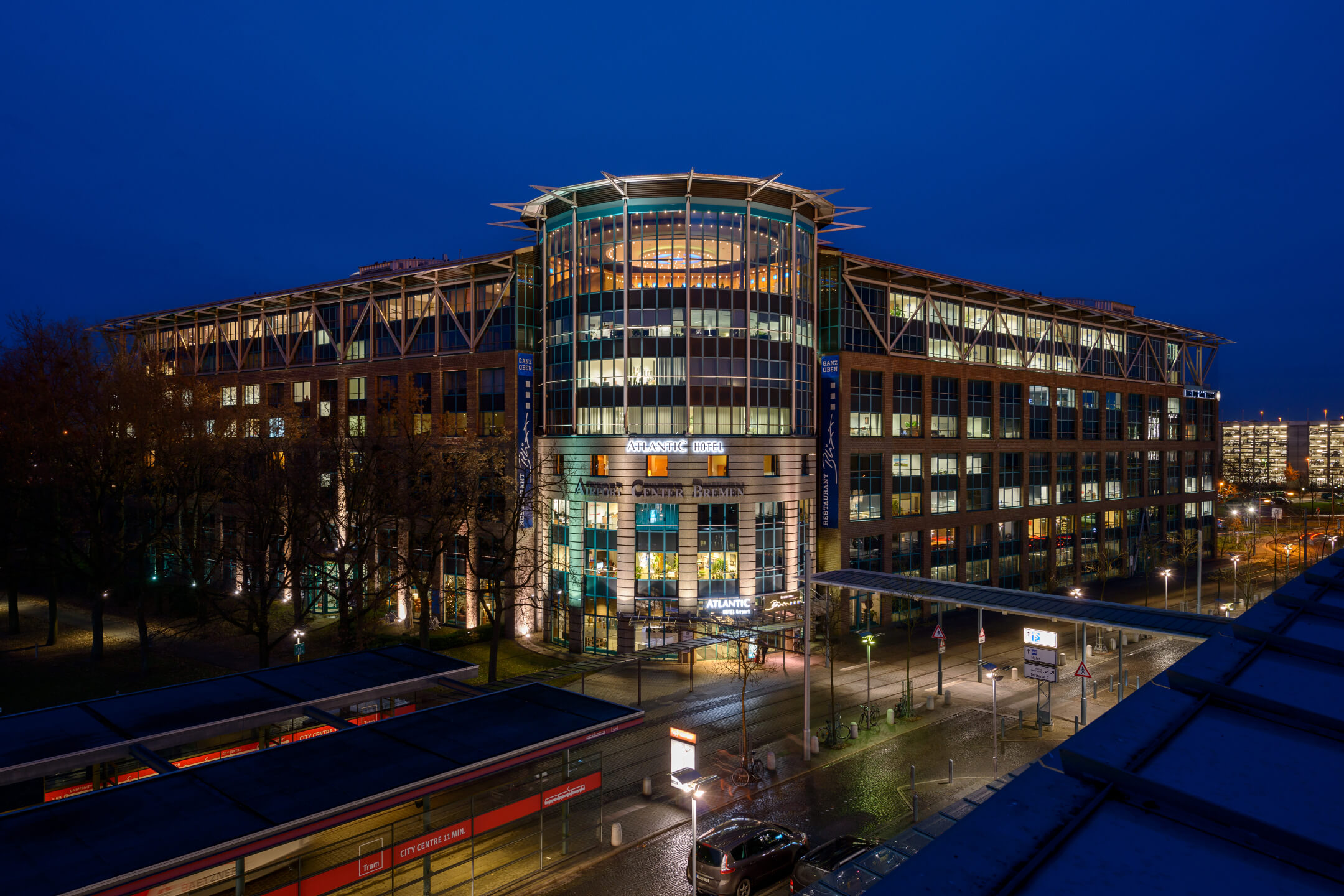 ATLANTIC Hotel Airport Bremen Ansicht bei Nacht ATLANTIC Hotel Airport bei Nacht, modernes Gebäude mit beleuchteten Fenstern und Eingangsbereich, blauer Himmel.