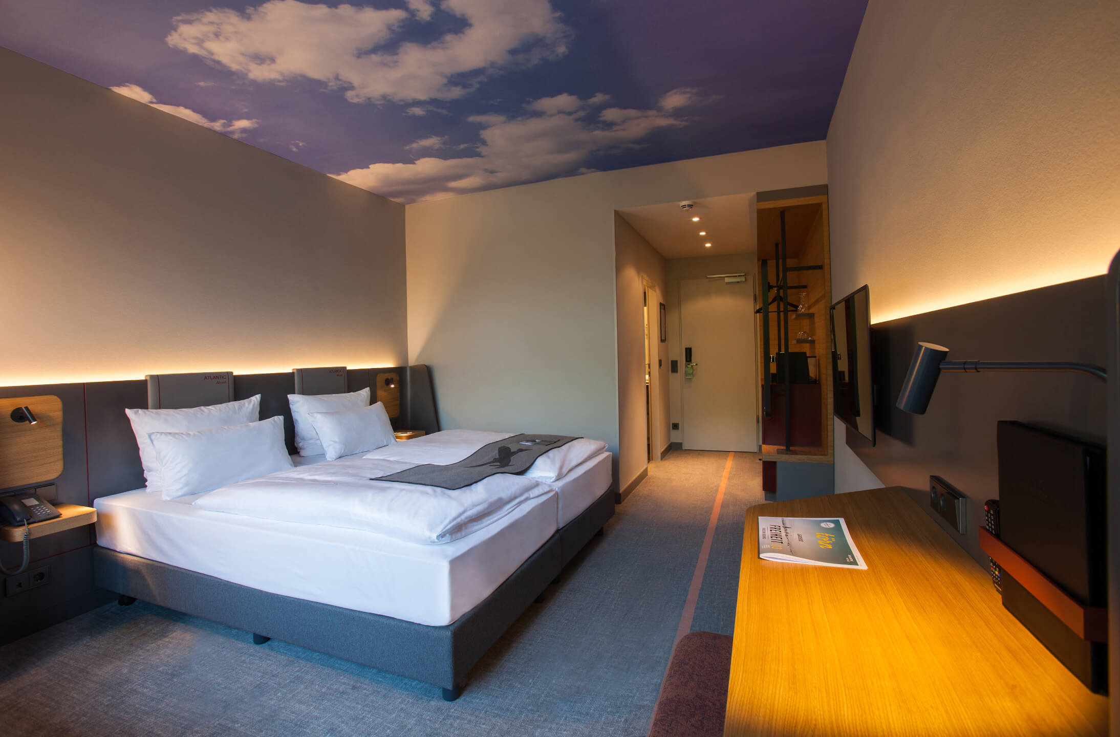 ATLANTIC Hotel Airport Bremen Business Zimmer Modernes Hotelzimmer mit Doppelbett, Schreibtisch und Himmelmotiv an der Decke im ATLANTIC Hotel Airport Bremen.