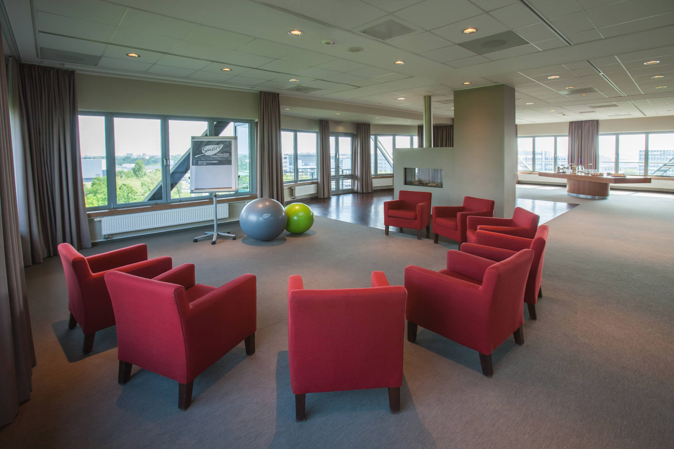 ATLANTIC Hotel Airport Bremen Veranstaltungsraum Lilienthal Heller Tagungsraum mit roten Sesseln im Kreis, Flipchart, Gymnastikbällen und großen Fenstern mit Blick ins Grüne.