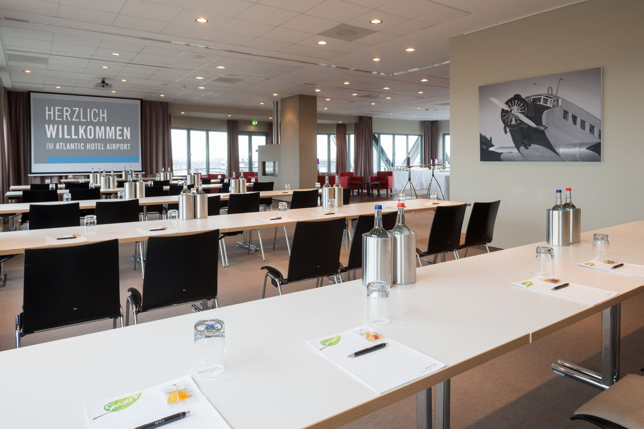 Veranstaltungsraum Lilienthal im ATLANTIC Hotel Airport Heller Konferenzraum im ATLANTIC Hotel Airport Bremen mit Tischen, Stühlen und Willkommensschild.