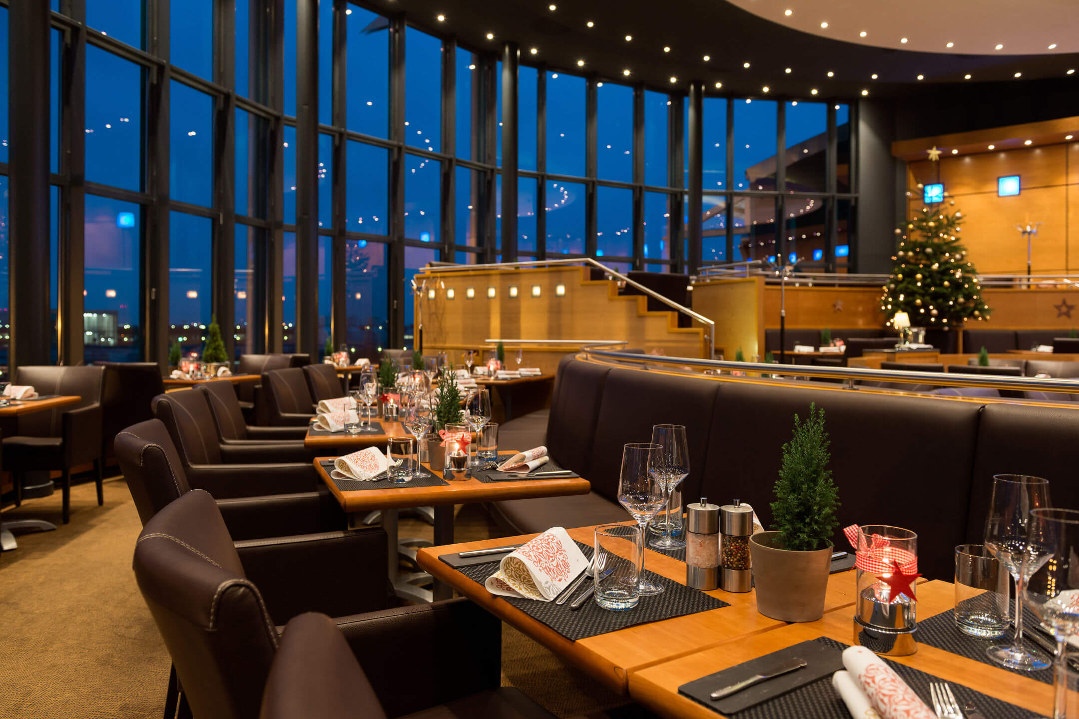 Weihnachtsstimmung im Restaurant BLIXX im ATLANTIC Hotel Airport Bremen Elegantes Restaurant im ATLANTIC Hotel Airport Bremen, festlich gedeckt mit Kerzen, großem Fenster und Weihnachtsbaum.