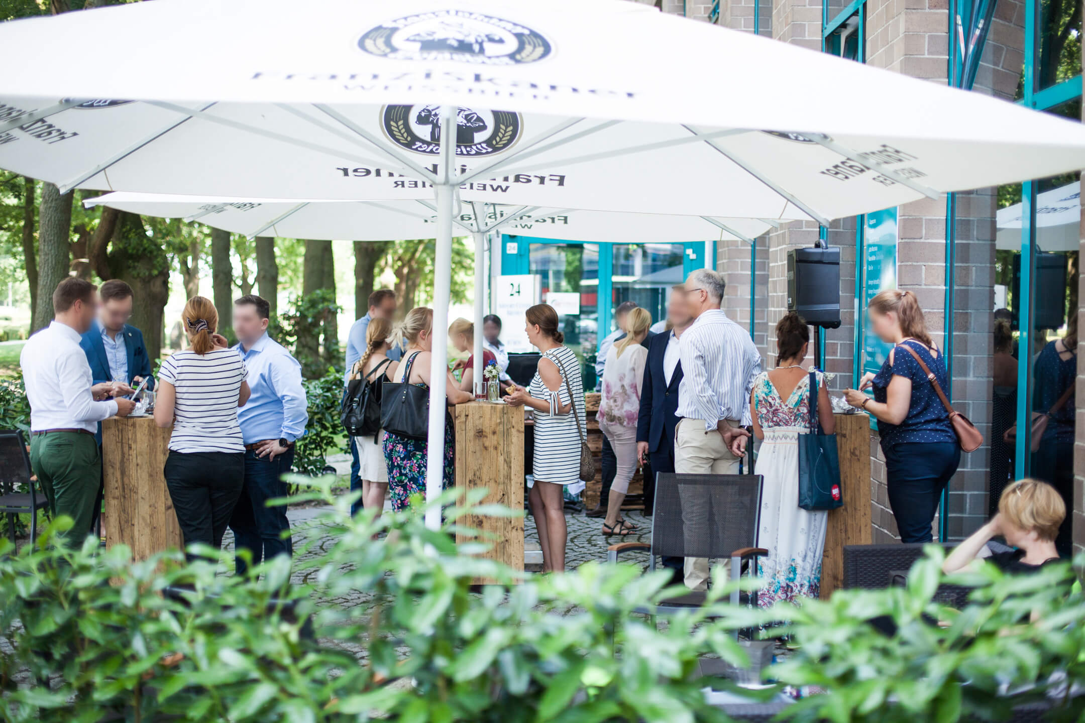 Terrasse des ATLANTIC Hotel Airport Bremen Personen genießen eine gesellige Veranstaltung im Freien unter großen weißen Sonnenschirmen am ATLANTIC Hotel Airport.