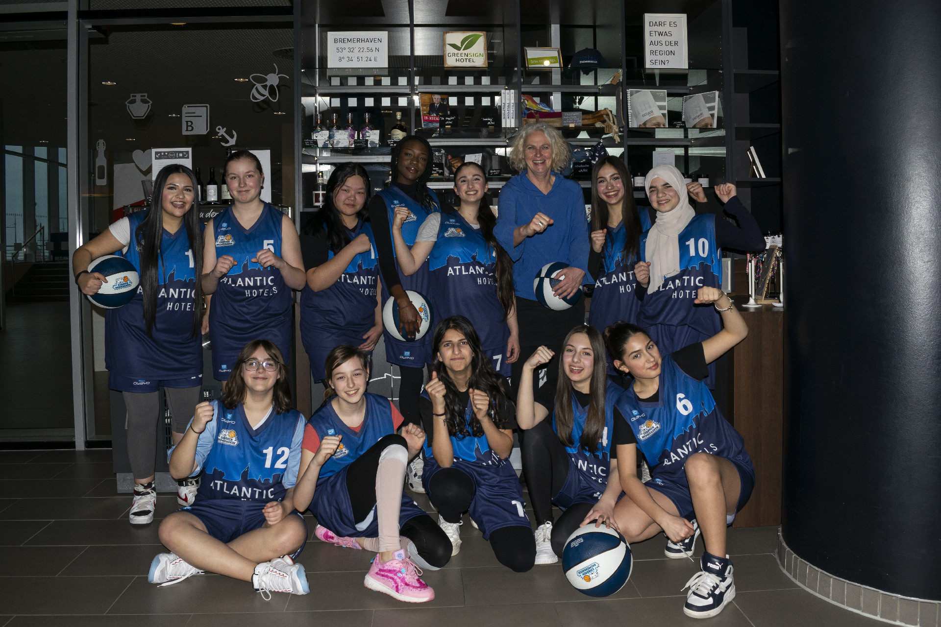 Teambild der Eisbären Bremerhaven U14 Mädchenmanschaft Jugend-Basketballteam posiert in blauen Trikots mit Basketballs im ATLANTIC Hotel Sail City, Bremerhaven.