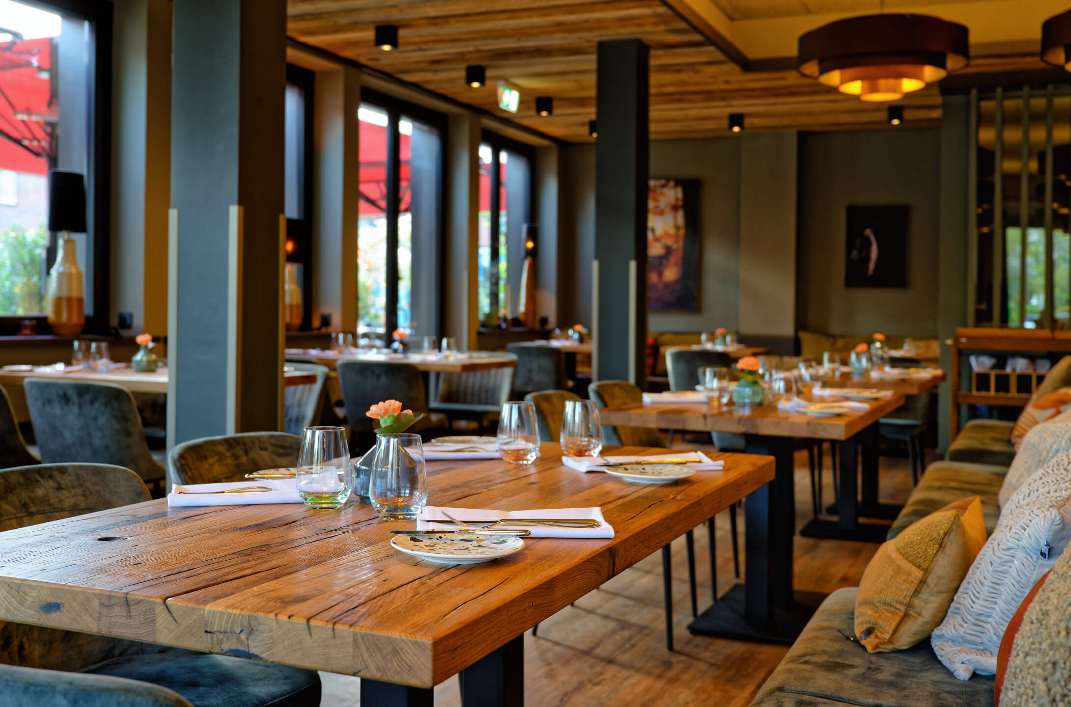 Restaurant CHALET im ATLANTIC Hotel Landgut Horn Bremen Gemütliches Restaurant mit Holztischen, gedeckt mit Gläsern und Tellern, warme Beleuchtung, große Fenster.