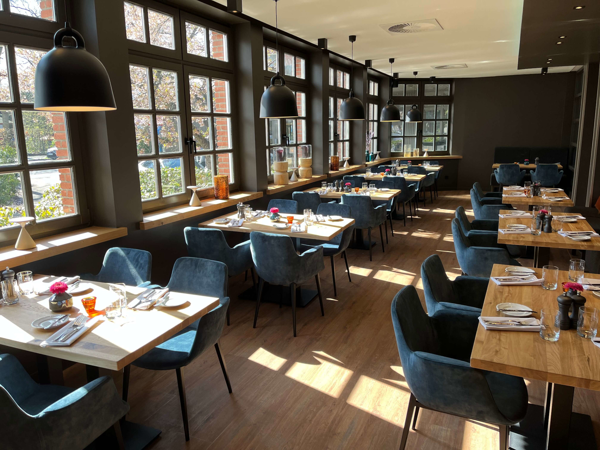 Restaurant VICTORIAN im ATLANTIC Hotel Landgut Horn Bremen Helles Restaurant mit Holztischen, blauen Stühlen und großen Fenstern im ATLANTIC Hotel Landgut Horn Bremen.