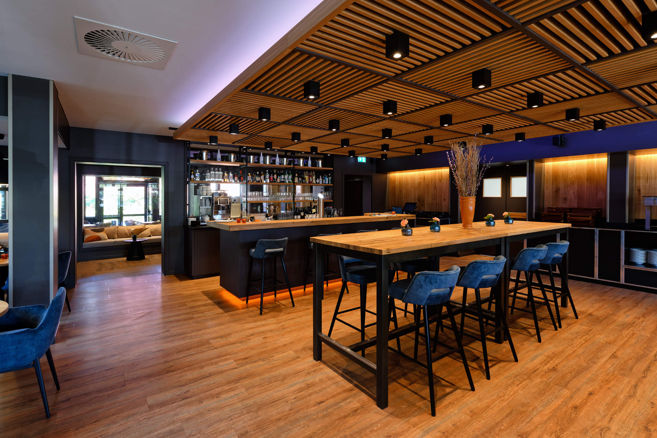 Modernes Restaurant VICTORIAN im ATLANTIC Hotel Landgut Horn Moderne Hotelbar mit Holztischen, blauen Stühlen, stimmungsvoller Beleuchtung und gut bestückter Rückwand.