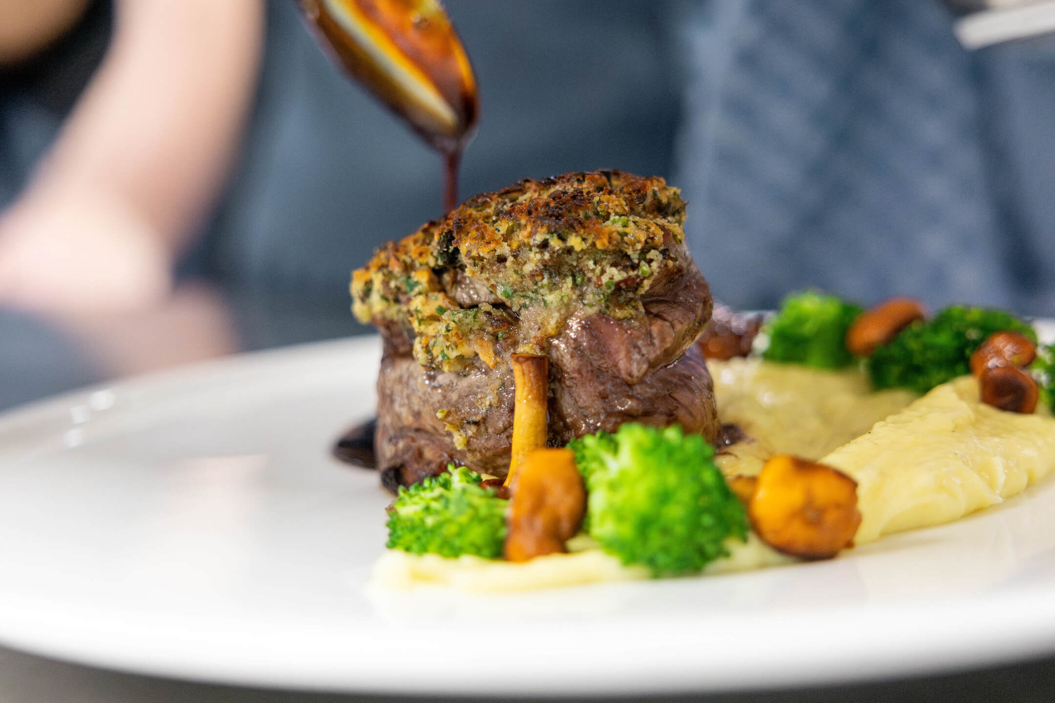 Essen im ATLANTIC Hotel Landgut Horn Bremen Gourmetgericht mit Fleisch, Brokkoli, Pilzen und Püree auf weißem Teller, mit dunkler Sauce garniert.