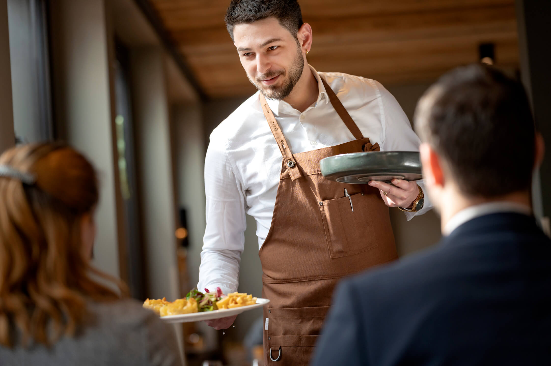 Moderne Restaurants im ATLANTIC Hotel Landgut Horn Bremen Kellner im ATLANTIC Hotel Landgut Horn serviert lächelnd Speisen an Gäste in elegantem Restaurantambiente.