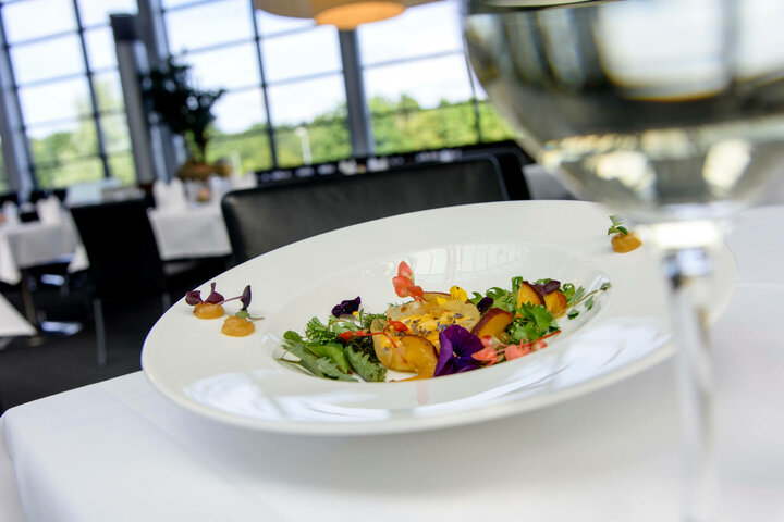 Essen im Restaurant gottlieb Ein elegantes Gericht mit essbaren Blüten auf weißem Teller in modernem Restaurant, im Vordergrund ein Glas Wein.
