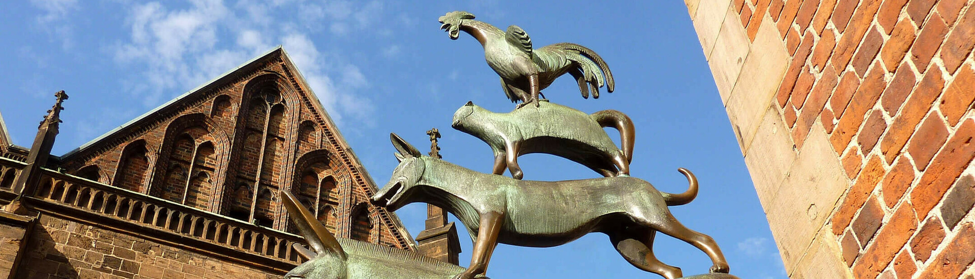 Die Bremer Stadtmusikanten Bronzestatue der Bremer Stadtmusikanten vor historischer Backsteinfassade, blauer Himmel im Hintergrund.