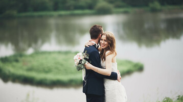 Hochzeit ATLANTIC Hotel Universum Ein Brautpaar umarmt sich vor einem See, die Braut hält einen Blumenstrauß.