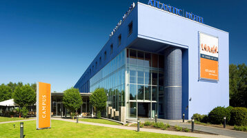 Außenansicht ATLANTIC Hotel Universum Modernes Hotelgebäude mit blauer Fassade und Glasfront, umgeben von Grünflächen und Bäumen.