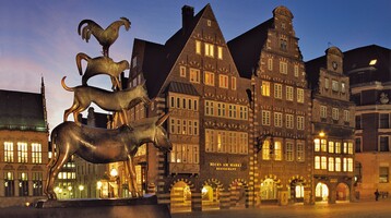 Bremer Marktplatz mit Statue der Bremer Stadtmusikanten Bronzestatue der Bremer Stadtmusikanten vor historischen Gebäuden im Abendlicht.