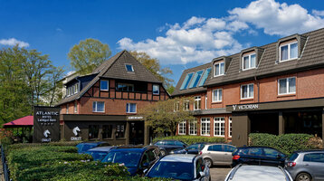 Außenansicht ATLANTIC Hotel Landgut Horn Bremen Backstein-Hotelgebäude mit Schrägdach, Parkplatz und grüner Umgebung unter blauem Himmel.