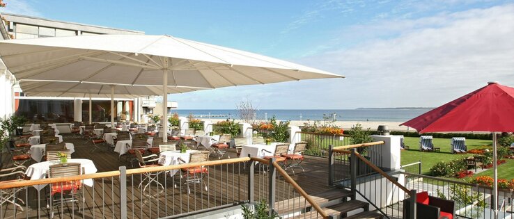 ATLANTIC Grand Hotel Travemünde Terrasse mit Blick auf die Ostsee Hotelterrasse mit Tischen und Stühlen, Blick auf die Ostsee, Sonnenschirme, gepflegter Garten mit Strandkörben.