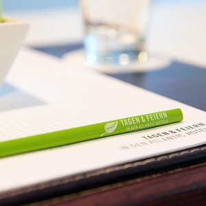 Stift und Zettel im Stil des SMART tagen & feiern Grüner Stift und Block mit "Tagen & Feiern" Aufschrift auf einem Konferenztisch, daneben ein Glas Wasser und eine Schale.