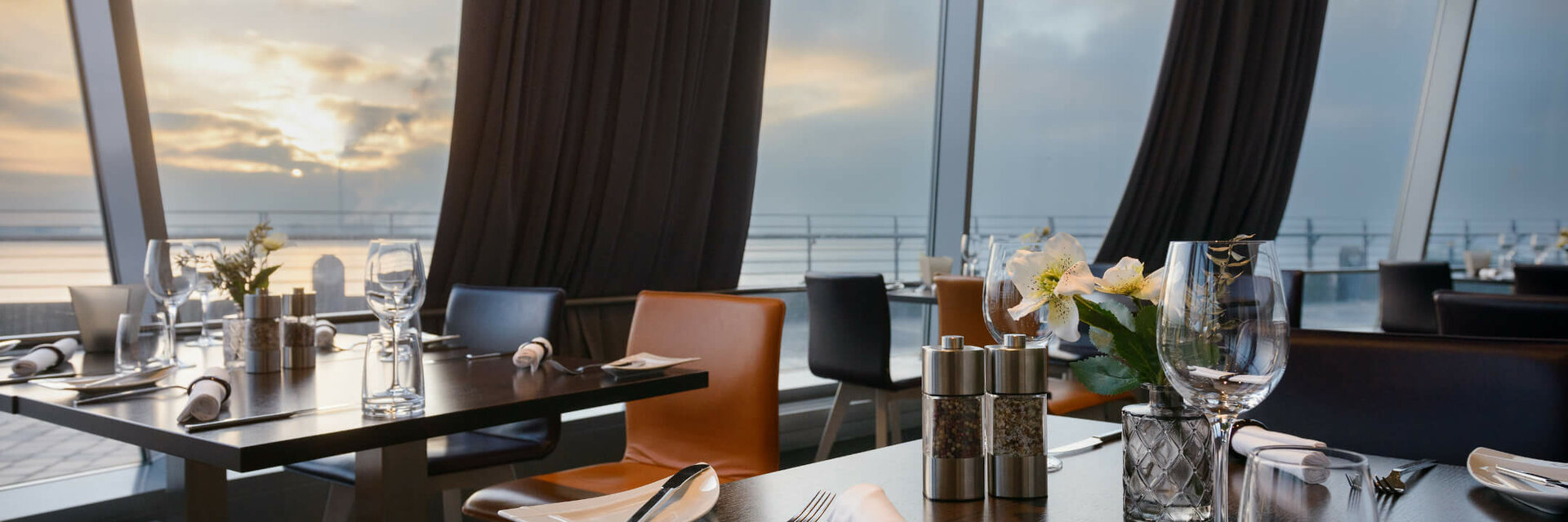 Restaurant Strom im ATLANTIC Hotel Sail City Modernes Restaurant mit gedeckten Tischen und Meerblick bei Sonnenuntergang im ATLANTIC Hotel Sail City, Bremerhaven.