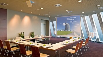 Hier tagen und feiern Sie in weltoffener Atmosphäre direkt am Deich mit Blick auf die Weser Heller Konferenzraum im ATLANTIC Hotel Sail City mit U-förmiger Bestuhlung und Blick auf eine Leinwand.