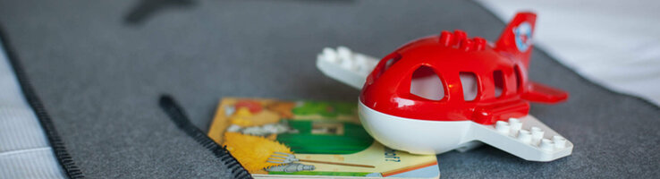 ATLANTIC Hotel Airport Bremen Familien Special Spielzeugflugzeug und Kinderbuch auf grauer Bettdecke im ATLANTIC Hotel Airport Bremen.