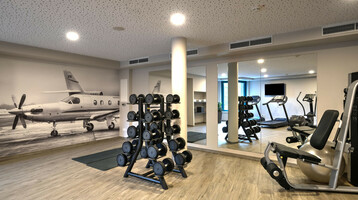 Fitnessbereich ATLANTIC Hotel Airport Bremen Fitnessraum im ATLANTIC Hotel Airport Bremen mit Hanteln, Fitnessgeräten und Flugzeugbild an der Wand.