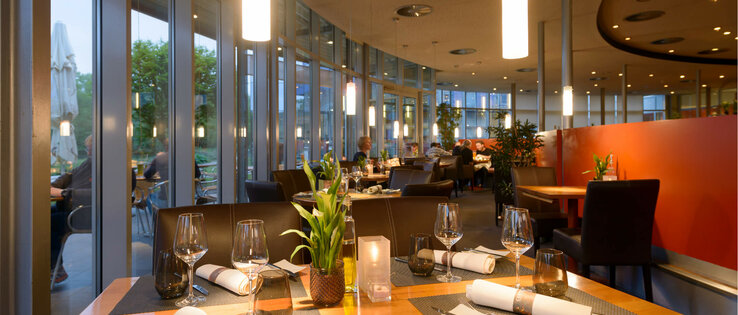 Restaurant CAMPUS des ATLANTIC Hotel Universum in Bremen Modernes Hotelrestaurant mit gedeckten Tischen, großen Fenstern und stimmungsvoller Beleuchtung im ATLANTIC Hotel Universum.