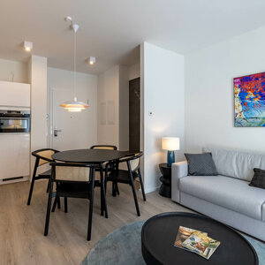 Wohnbereich in der Kategorie Appartement in der ATLANTIC Dependance | ATLANTIC Grand Hotel Travemünde Modernes Hotelzimmer mit Küche, Esstisch, Sofa und bunter Wandkunst im ATLANTIC Grand Hotel Travemünde.