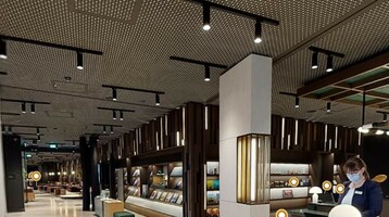 Moderne Hotel-Lobby mit Empfangstresen, beleuchtetem Regal und Mitarbeiterin mit Maske.