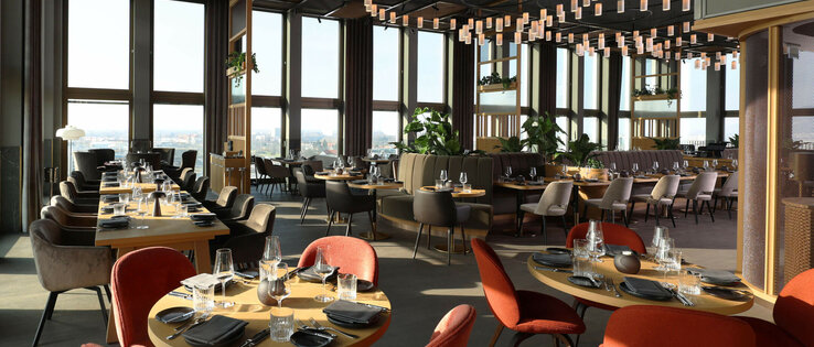 Restaurant 15 High in der 15. Etage im ATLANTIC Hotel Heidelberg Modernes Hotelrestaurant mit eleganten Holztischen, roten und grauen Stühlen, großen Fenstern und stilvollen Hängelampen.