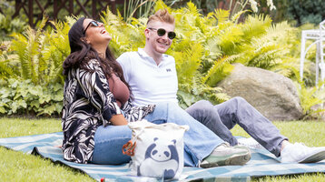 ATLANTIC Hotel Landgut Horn Angebote im Grünen Ein Paar sitzt auf einer Picknickdecke im grünen Garten vom ATLANTIC Hotel Landgut Horn