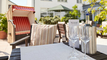 Terrasse des ATLANTIC Hotel Vegesack Terrasse des ATLANTIC Hotel Vegesack mit Strandkorb, gedecktem Tisch und Weinflasche im Freien.