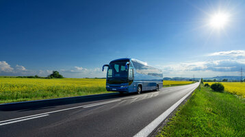Gruppenreisen im ATLANTIC Hotel Vegesack Reisebus auf Landstraße, umgeben von gelben Feldern unter blauem Himmel mit Sonne.