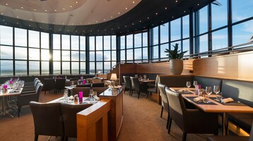 Restaurant BLIXX im ATLANTIC Hotel Airport in Bremen Modernes Restaurant mit Panoramafenstern, elegant gedeckten Tischen und Blick auf den Sonnenuntergang am Flughafen Bremen.