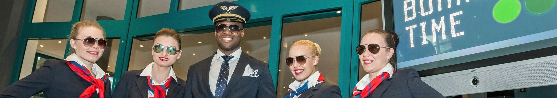 Team des ATLANTIC Hotel Airport in Bremen Hotelpersonal in Uniformen posiert lächelnd vor dem Eingang des ATLANTIC Hotel Airport Bremen.