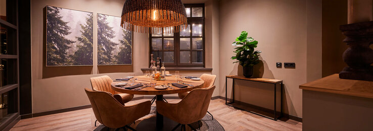 Corner im Restaurant Chalet im ATLANTIC Hotel Landgut Horn Bremen Gemütlicher Essbereich im ATLANTIC Hotel Landgut Horn, mit Holztisch, vier Stühlen, großer Lampe und Naturbildern an der Wand.