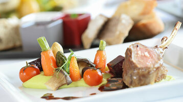 Restaurant Holstein's Gourmetgericht mit Lammkarree, buntem Gemüse und Sauce kunstvoll auf weißem Teller im ATLANTIC Grand Hotel Travemünde.