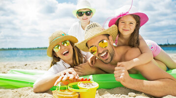 ATLANTIC Grand Hotel Travemünde – Familie am Strand © drubig photo – Fotolia Familie am Strand mit Sonnenhüten und Sonnenbrillen, lachend auf einer Luftmatratze liegend, Sandspielzeug im Vordergrund.