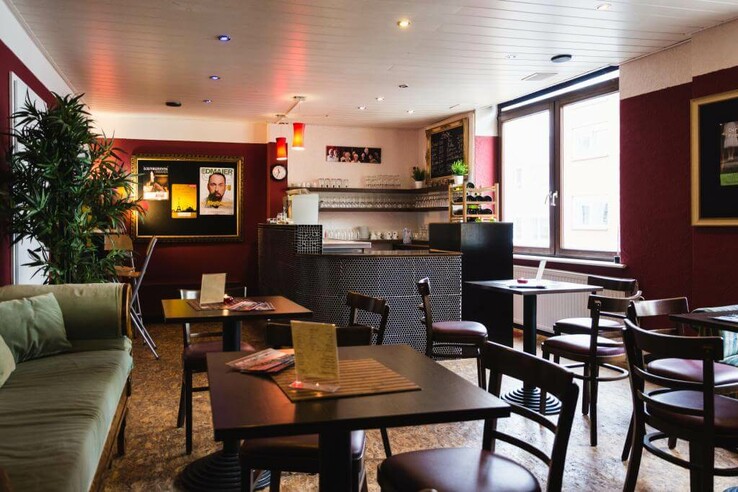 Schnürschuh Theater Bremen Gemütliche Hotelbar mit Holztischen, Stühlen, Sofa, Barbereich und großen Fenstern, dekoriert mit Pflanzen und Bildern. Schnürschuh Theater Bremen