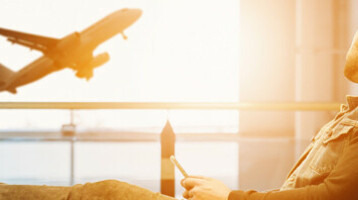 Mann schaut Flugzeug nach Mann entspannt im Flughafen, schaut auf startendes Flugzeug durch großes Fenster.