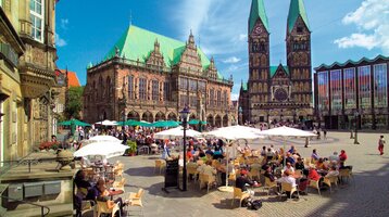 Bremer Marktplatz mit Rathaus im Hintergrund Blick auf den belebten Bremer Marktplatz mit Rathaus, Dom und Außencafés unter Sonnenschirmen.