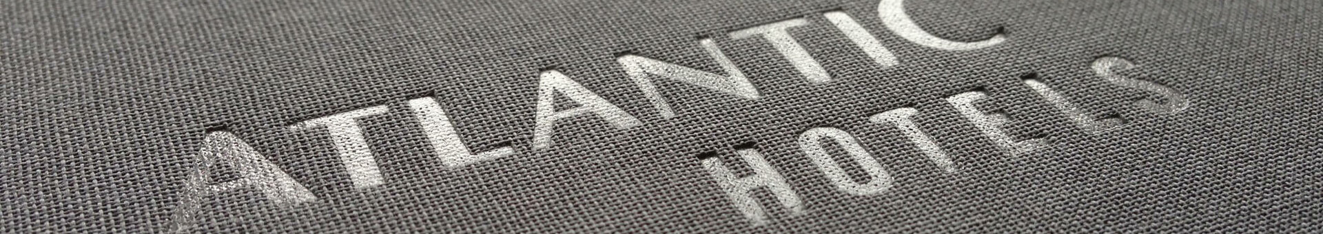 Prägelogo "Atlantic Hotels" auf grauer Stoffoberfläche.