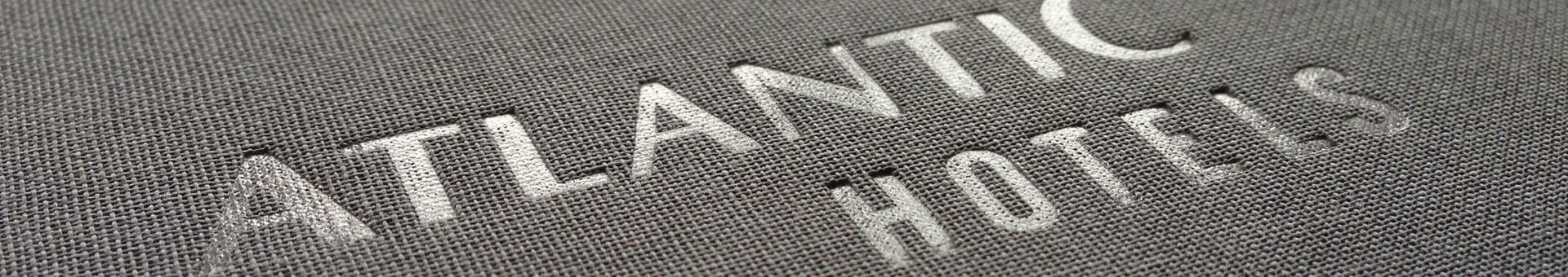 Prägelogo "Atlantic Hotels" auf grauer Stoffoberfläche.