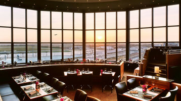 Restaurant BLIXX im ATLANTIC Hotel Airport in Bremen Restaurant mit Panoramafenstern, Blick auf Flughafen und Sonnenuntergang, elegant gedeckte Tische im ATLANTIC Hotel Airport Bremen.