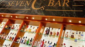 ATLANTIC Hotel Wilhelmshaven Seven C´s Bar Regal mit beleuchteten Spirituosenflaschen unter dem Schild "Seven Cs Bar" auf dunklem Hintergrund.