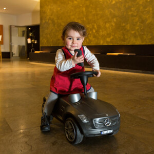 Kleines Mädchen flitzt durch die Hotellobby auf einem Spielzeug-Mercedes Kleines Mädchen flitzt durch die Hotellobby auf einem Spielzeug-Mercedes