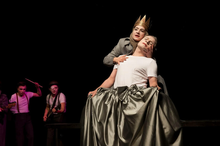 © bremer shakespeare company Theaterszene mit Schauspieler in Krone, der einen anderen umarmt; Musiker im Hintergrund. © bremer shakespeare company