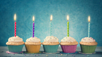 ATLANTIC Hotels Gutscheine Fünf bunte Cupcakes mit brennenden Kerzen vor blauem Hintergrund.