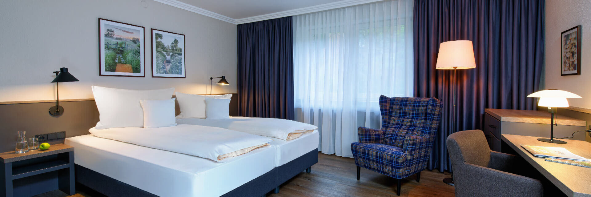 Comfort Plus Doppelzimmer im ATLANTIC Hotel Landgut Horn Helles Hotelzimmer mit Doppelbett, Schreibtisch, Sessel, Holzboden und großen Fenstern mit Vorhängen im ATLANTIC Hotel.