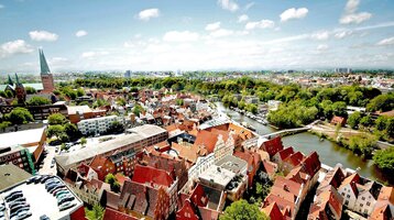 Die Dächer Lübecks von oben fotografiert Blick auf Lübecks Altstadt mit roten Ziegeldächern, Kirchtürmen und Fluss bei klarem Himmel.