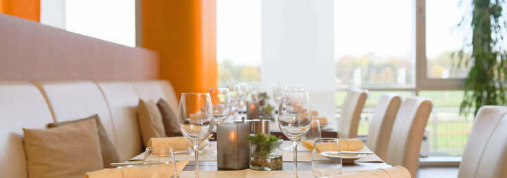 Restaurant Derby Elegantes Restaurant mit gedecktem Tisch, weißen Stühlen und Blick auf Grünflächen im ATLANTIC Hotel Galopprennbahn Bremen.