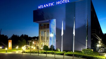 Außenansicht des ATLANTIC Hotel Universum Bremen bei Nacht ATLANTIC Hotel Universum bei Nacht, beleuchtete Fassade, drei Fahnenmasten, gepflegter Eingangsbereich.